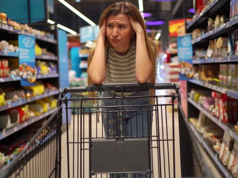 Young woman standing among the produce aisle at the supermarket and feeling worried about the increase in food prices